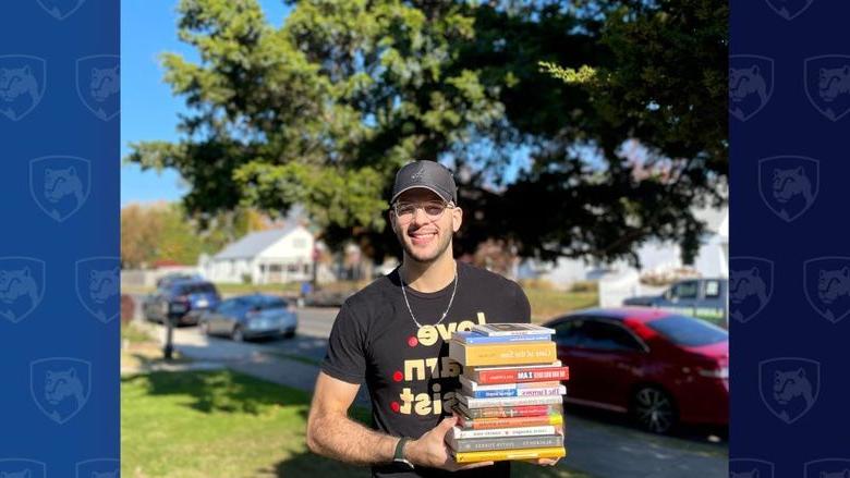 Man holding stack of books in front of a tree